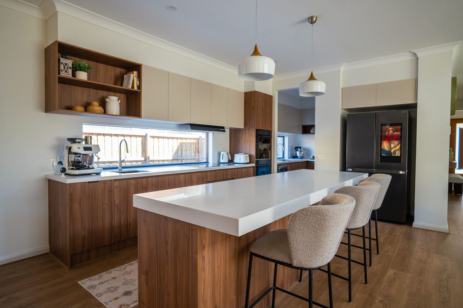 The finished Officer kitchen: timber joinery, a stone island with stools, and a window behind the sink in place of a tiled splashback.